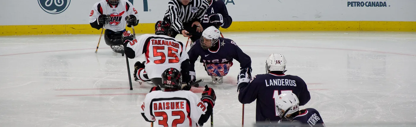 Photo of Ice Sled Hockey team United States (blue shirts) vs Japan (white shirts) during the 2010 Paralympics in Vancouver. Credit: By popejon2 via Wikimedia Commons.