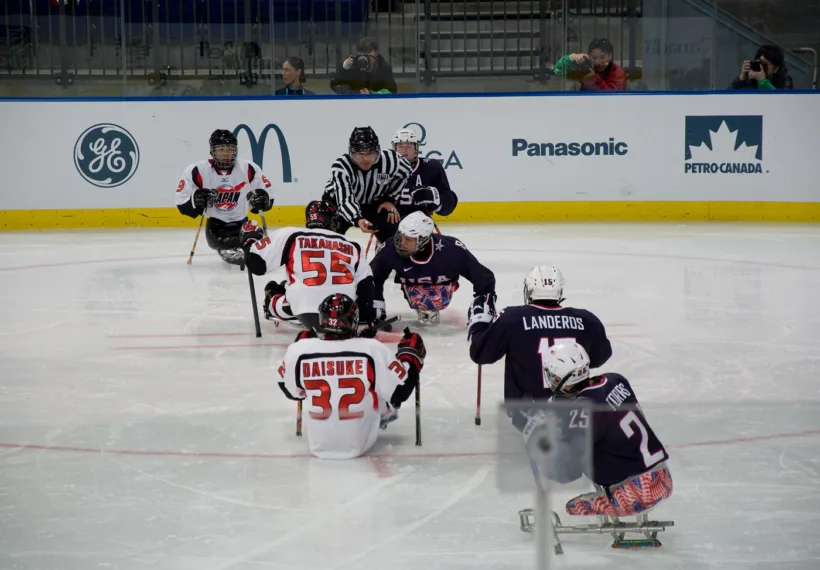 Photo of Ice Sled Hockey team United States (blue shirts) vs Japan (white shirts) during the 2010 Paralympics in Vancouver. Credit: By popejon2 via Wikimedia Commons.