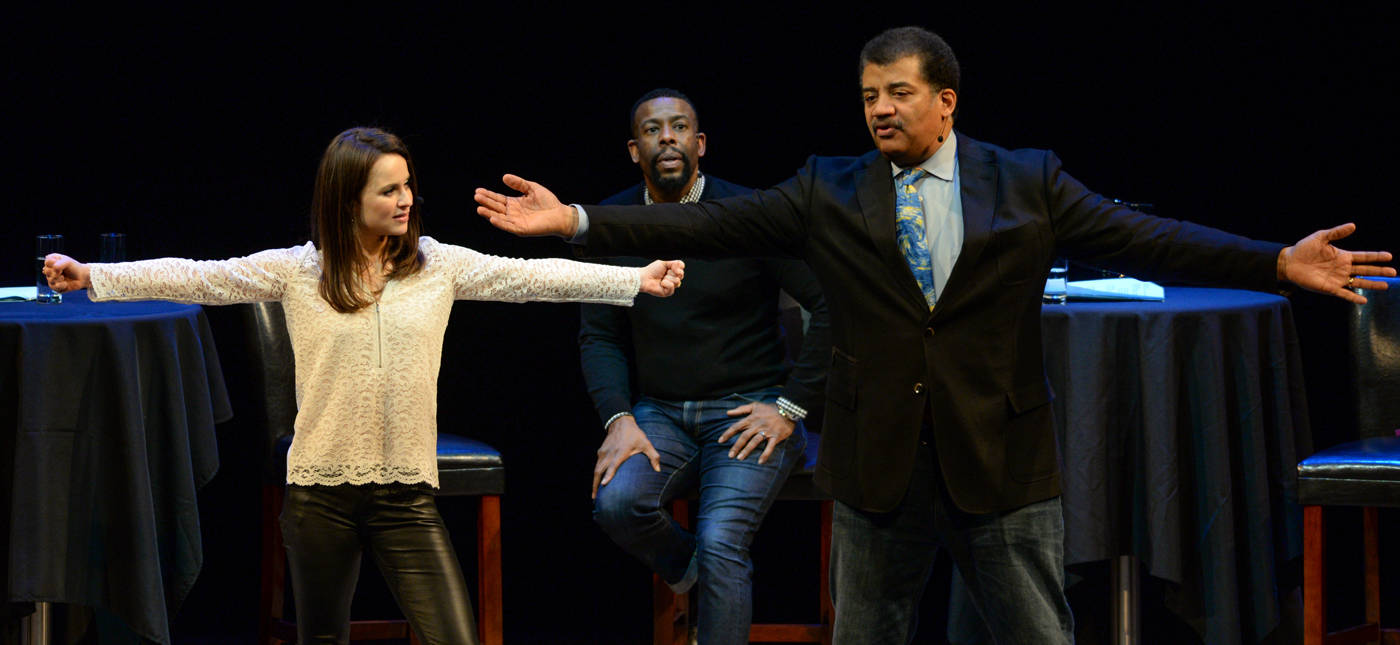 Elliot Severn’s photo of Sasha Cohen and Neil deGrasse Tyson demonstrate spins onstage at BAM, while host Chuck Nice looks on.