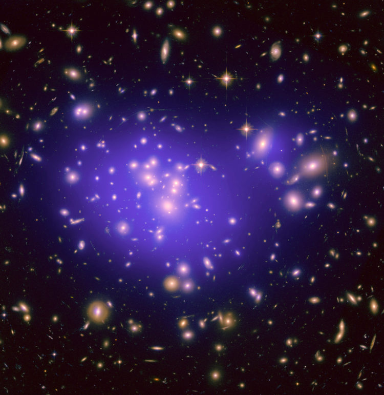 NASA’s image shows the galaxy cluster Abell 1689, with the mass distribution of the dark matter in the gravitational lens overlaid (in purple). The mass in this lens is made up partly of normal (baryonic) matter and partly of dark matter. Distorted galaxies are visible around the edges of the gravitational lens.