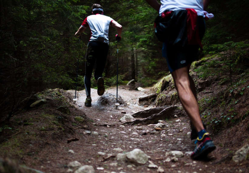 Two men viewed from behind as they run up a mountain trail.