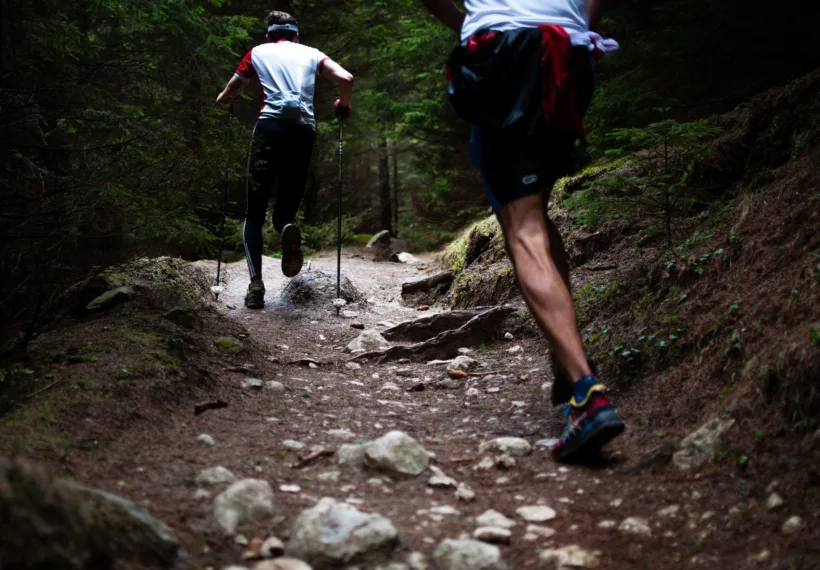 Two men viewed from behind as they run up a mountain trail.