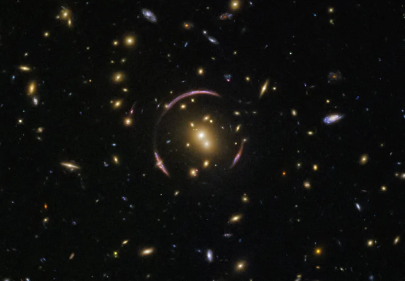 These graceful arcs are examples of a cosmic phenomenon known as an Einstein ring. The ring is created as the light from a distant objects, like galaxies, pass by an extremely large mass, like this galaxy cluster. In this image, the light from a background galaxy is diverted and distorted around the massive intervening cluster and forced to travel along many different light paths towards Earth, making it seem as though the galaxy is in several places at once.