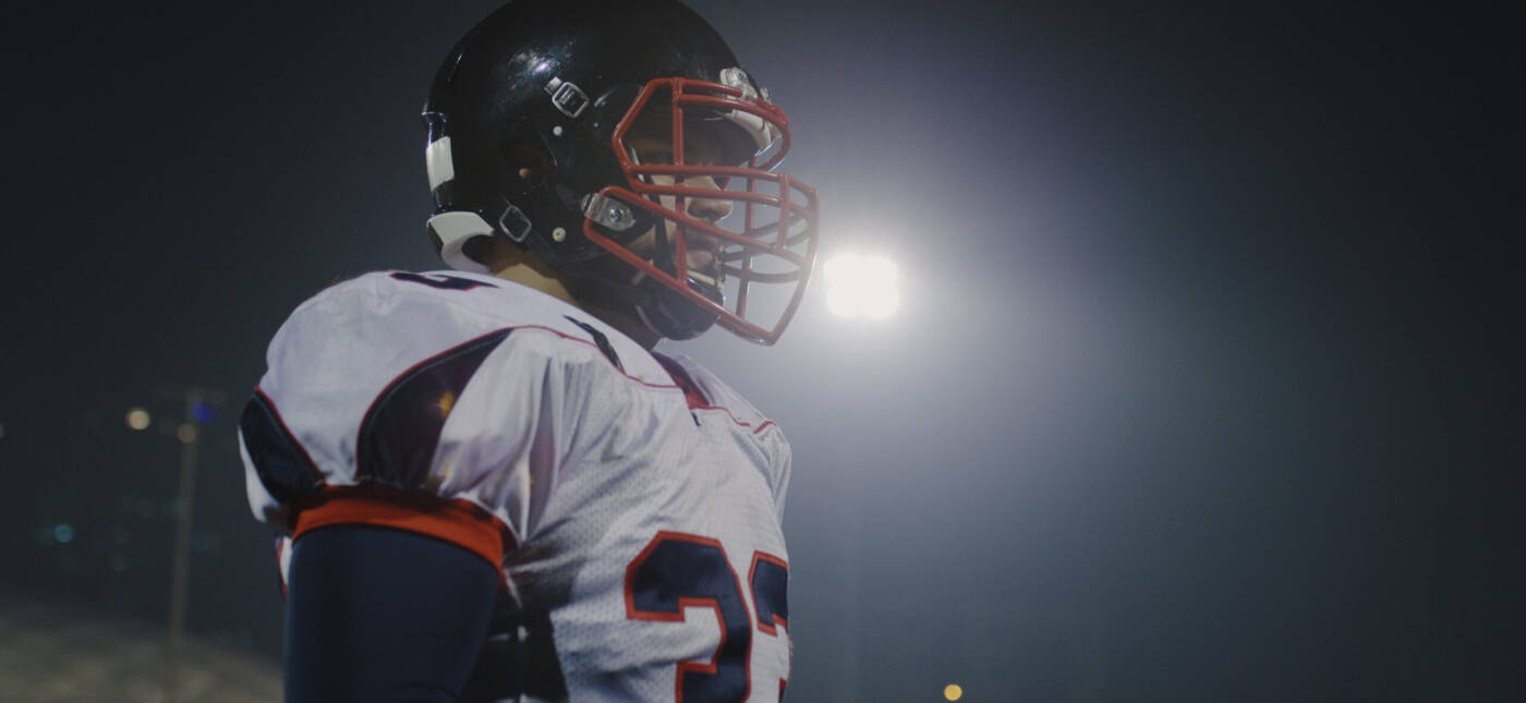 Portrait Of A Confident Football Player Standing On The Field At Night