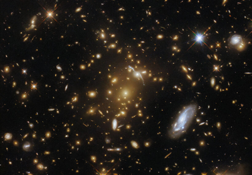 A vast galaxy cluster lurks in the centre of this image from the NASA/ESA Hubble Space Telescope. Like a submerged sea monster causing waves on the surface, this cosmic leviathan can be identified by the distortions in spacetime around it. The mass of the cluster has caused the images of background galaxies to be gravitationally lensed; the galaxy cluster has caused a sufficient curvature of spacetime to bend the path of light and cause background galaxies to appear distorted into streaks and arcs of light. A host of other galaxies can be seen surrounding the cluster, and a handful of foreground stars with tell-tale diffraction spikes are scattered throughout the image.This particular galaxy cluster is called eMACS J1823.1+7822, and lies almost nine billion light-years away in the constellation Draco. It is one of five exceptionally massive galaxy clusters explored by Hubble in the hopes of measuring the strengths of these gravitational lenses and providing insights into the distribution of dark matter in galaxy clusters. Strong gravitational lenses like eMACS J1823.1+7822 can help astronomers study distant galaxies by acting as vast natural telescopes which magnify objects that would otherwise be too faint or distant to resolve.