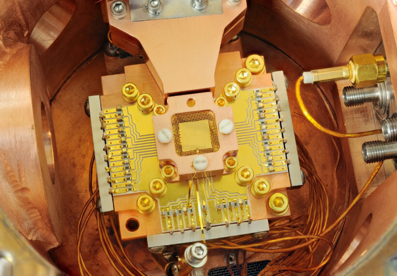 NIST physicists used this apparatus to coax two beryllium ions (electrically charged atoms) into swapping the smallest measurable units of energy back and forth, a technique that may simplify information processing in a quantum computer. The ions are trapped about 40 micrometers apart above the square gold chip in the center. The chip is surrounded by a copper enclosure and gold wire mesh to prevent buildup of static charge.