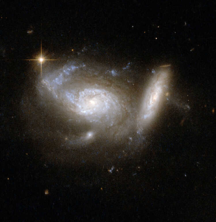 ESO 550-2 shows a pair of spiral galaxies, the larger nearly face-on and accompanied by a smaller, highly tilted partner. Tidal interaction from the smaller companion has clearly deformed one arm of the larger galaxy. Strong star formation continues both in the deformed arm and in a ring structure around the galaxy's core. The pair is surrounded by the glow of faintly shining stars and interstellar matter that has been smeared through space by the gravitational effects of the collision and the pull of a third nearby galaxy.