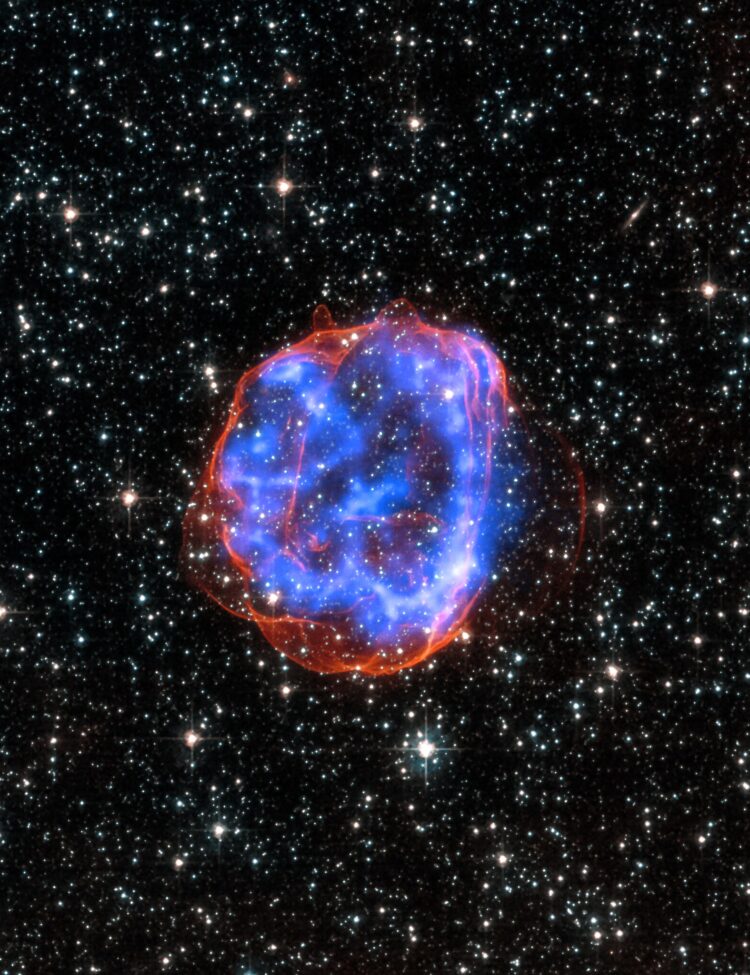 X-ray & Optical Images of SNR E0519-69.0 - When a massive star exploded in the Large Magellanic Cloud, a satellite galaxy to the Milky Way, it left behind an expanding shell of debris called SNR 0519-69.0. Here, multimillion degree gas is seen in X-rays from Chandra (blue). The outer edge of the explosion (red) and stars in the field of view are seen in visible light from Hubble.