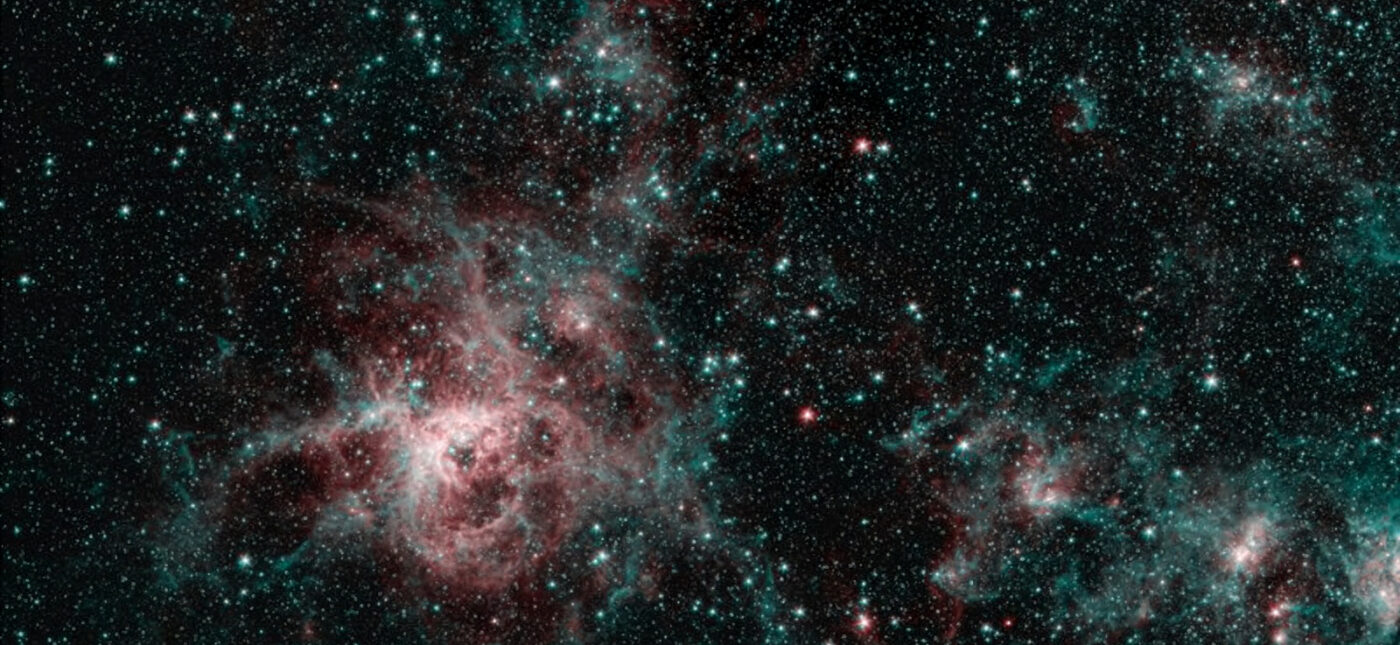 This image from NASA's Spitzer Space Telescope shows the Tarantula Nebula in two wavelengths of infrared light, each represented by a different color. The red color at the heart of the nebula shows the presence of particularly hot gas emitting infrared light at a wavelength of 4.5 micrometers. The blue regions are dust composed of molecules called polycyclic aromatic hydrocarbons (PAHs), which are also found in ash from coal, wood and oil fires on Earth. Regions emitting both wavelengths appear white.
